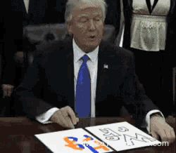 a man in a suit and tie is sitting at a table with a piece of paper on it that says ' donald trump '
