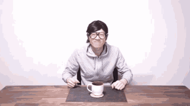 a man wearing glasses is sitting at a table with a cup of coffee
