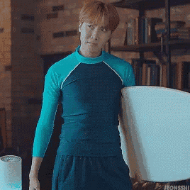 a man in a blue shirt is holding a surfboard in a room .