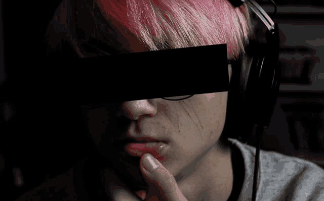 a person with pink hair is wearing headphones and has a black piece of paper over their eyes