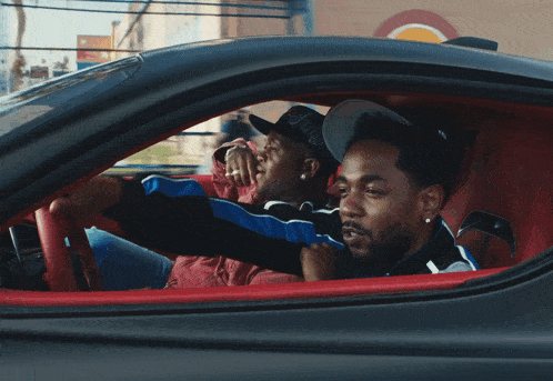 a man wearing a hat with the letter l on it is driving a car