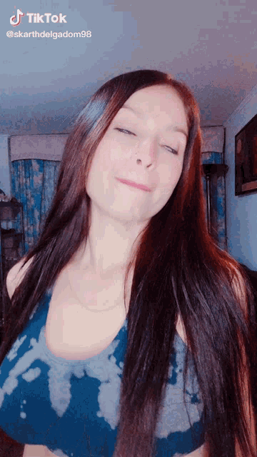 a woman with long hair is wearing a blue tie dye tank top and has a tiktok account