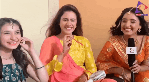 three women are sitting next to each other and smiling while holding a microphone .