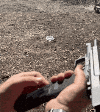 a person is holding a gun in their hands and a piece of paper is on the ground in the background