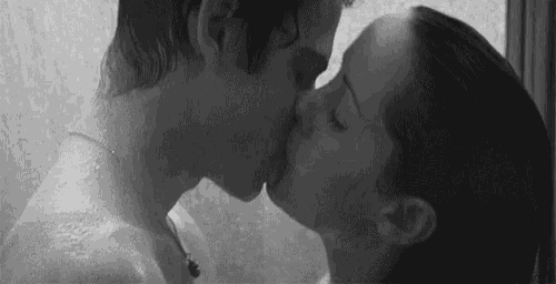 a black and white photo of a man and woman kissing in the shower .