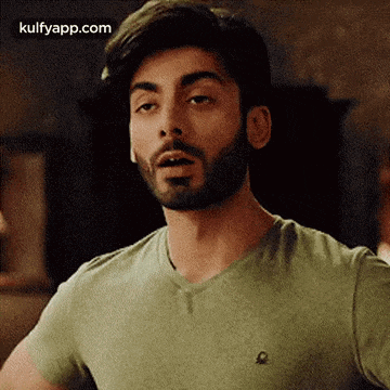a man with a beard is wearing a green t-shirt and looking at the camera .