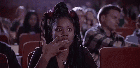 a woman is sitting in a theater watching a movie and making a face .