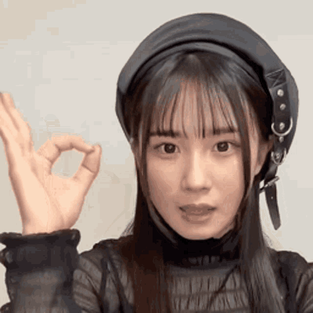 a young woman wearing a black hat and a black shirt is giving the ok sign .
