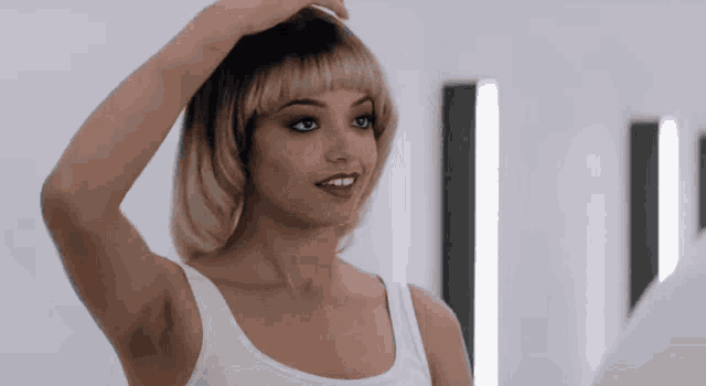 a woman in a white tank top is adjusting her hair