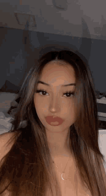 a woman with long brown hair and red lips is taking a selfie in a bedroom .
