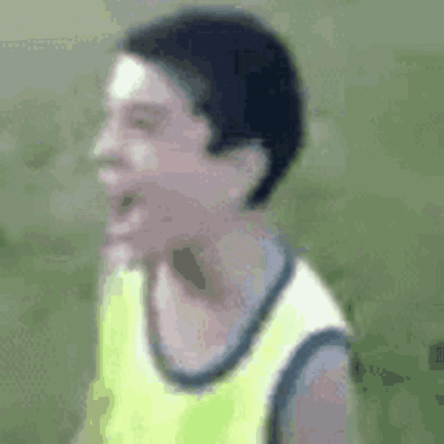 a young boy in a yellow vest is making a funny face while standing in the grass .