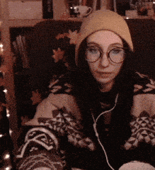 a woman wearing a beanie and glasses is sitting on a chair