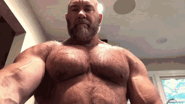 a bald man with a beard is taking a selfie with his muscles .