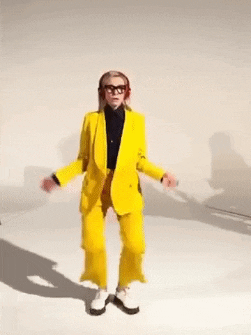 a woman in a yellow suit is dancing on a white surface .
