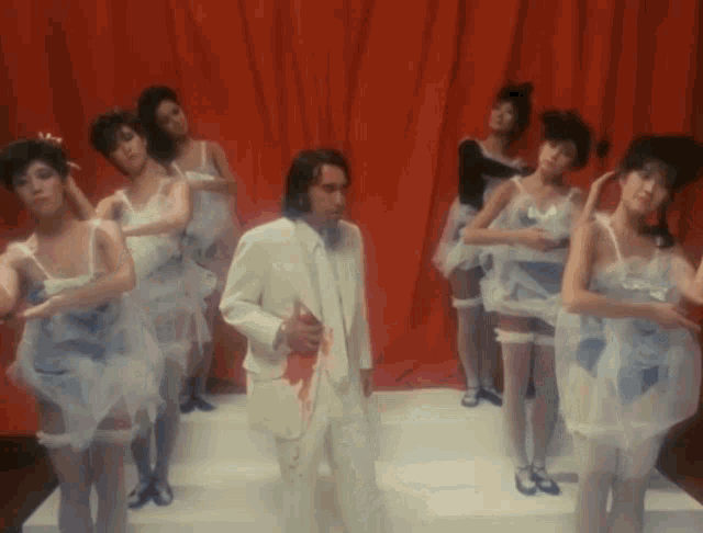 a man in a white suit is surrounded by women in white dresses and stockings