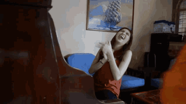 a woman is laughing in a living room with a painting of a ship on the wall behind her .