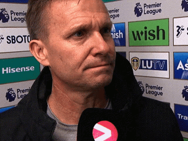 a man is holding a microphone in front of a wall that says premier league on it