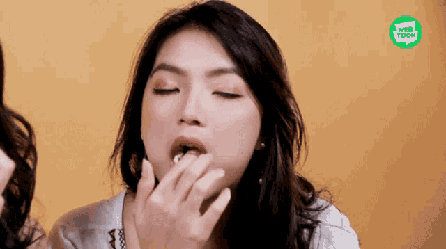 a woman is eating something with a web toon logo in the background