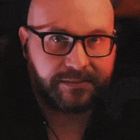 a bald man with a beard and glasses is looking at the camera .