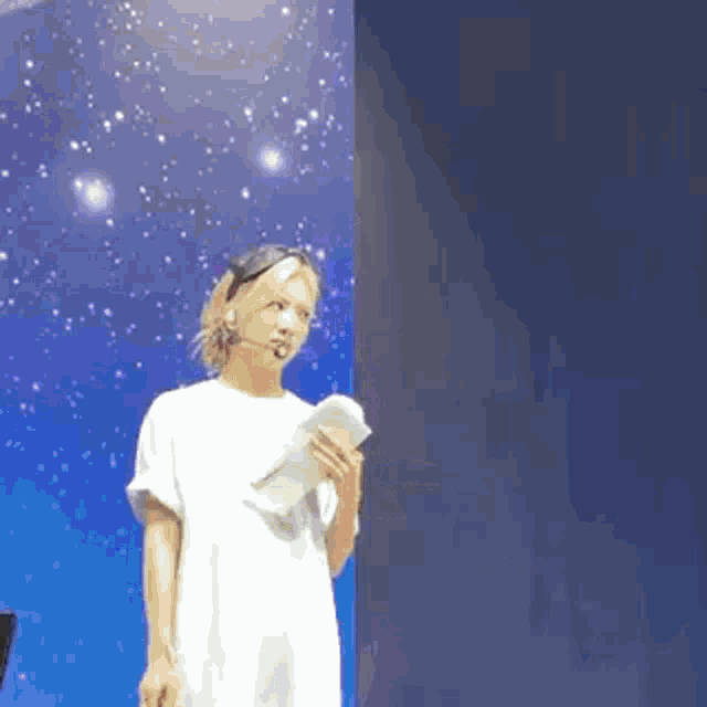 a woman in a white dress is standing in front of a blue wall holding a microphone .