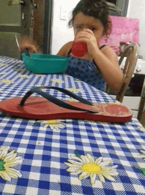 a little girl drinking from a red cup while sitting at a table