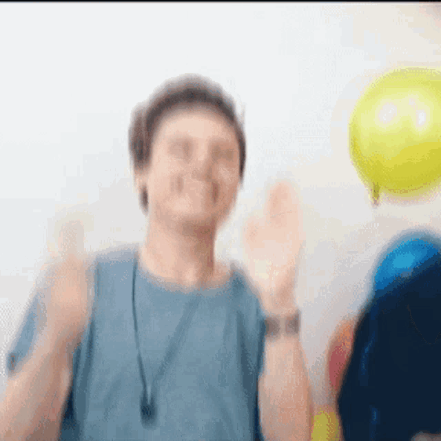 a man in a blue shirt is standing in front of balloons and making a funny face .