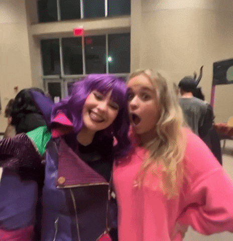 a couple of girls are posing for a picture together . one of the girls is wearing a purple wig .
