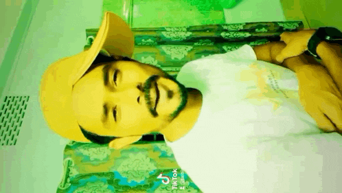 a man with a beard wearing a yellow hat and a white shirt is smiling .