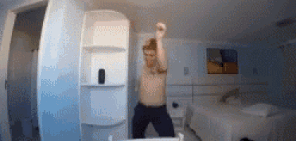 a man without a shirt is dancing in front of a mirror in a hotel room .