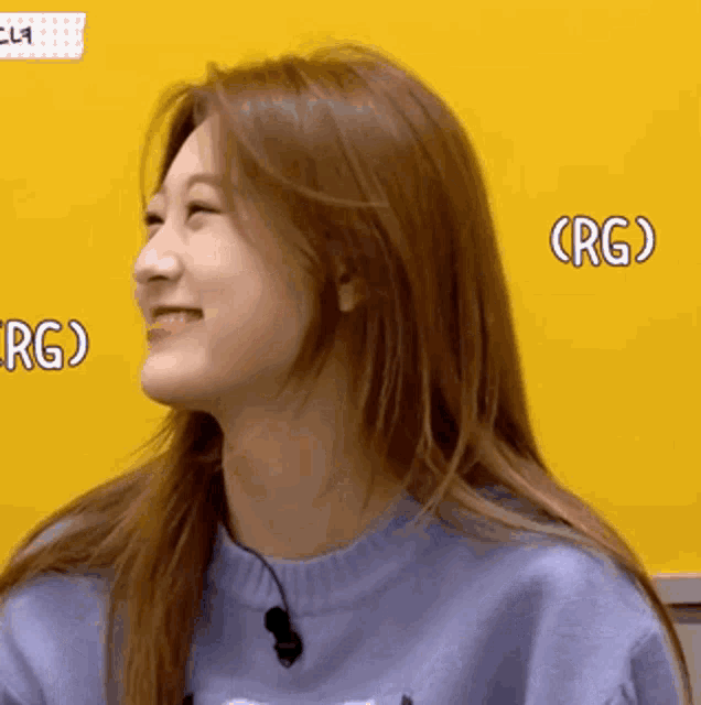 a woman wearing a blue sweater is smiling in front of a yellow board that says rgo