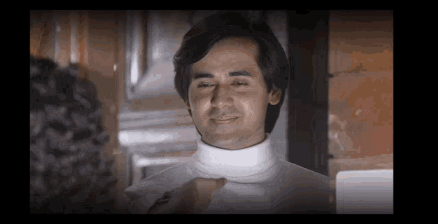 a man in a white turtleneck is smiling and looking at another man