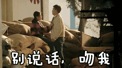 a man and woman are kissing in front of a pile of bags with chinese writing on the bottom
