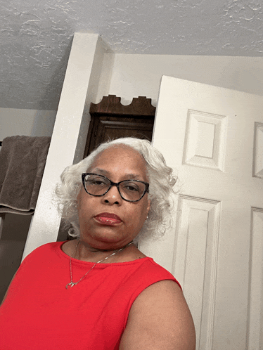a woman wearing glasses and a red top stands in front of a white door