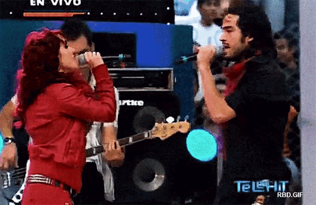 a woman singing into a microphone next to a man playing a guitar and a sign that says telehit