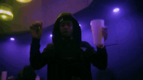 a man in a hooded jacket is holding a bottle of alcohol in his hands .