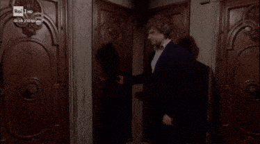 a man in a suit stands in front of a door that says rai 1 hd on it