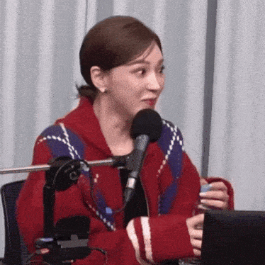 a woman in a red sweater is sitting in front of a microphone holding a glass of water .