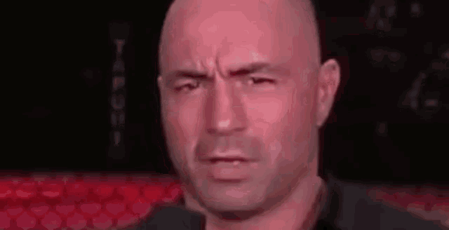 a bald man is making a funny face while standing in front of red seats .