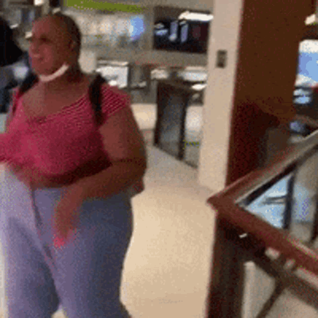 a woman in a pink top and blue pants is walking down a hallway