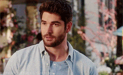a man with a beard wearing a blue shirt is standing in front of a building .