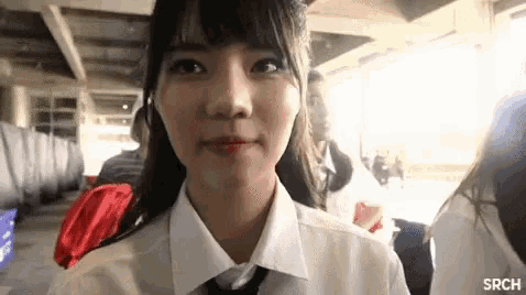 a girl in a white shirt and tie is looking at the camera and smiling .