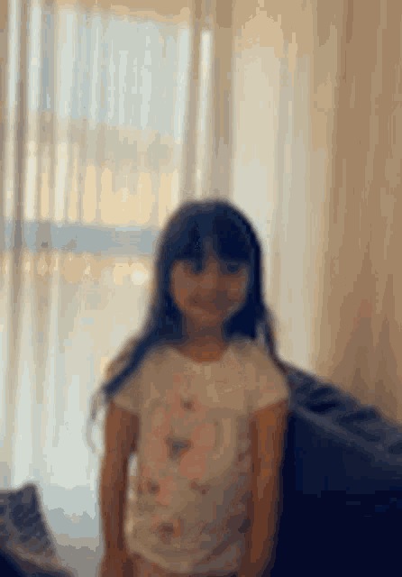 a little girl in a white shirt is standing in front of a window .