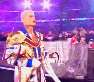 a wrestler in a robe is walking into a wrestling ring .
