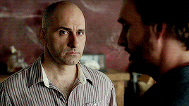 a bald man in a striped shirt is talking to another bald man in a black shirt .