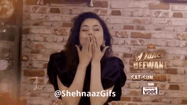 a woman is blowing a kiss with her hands in front of a brick wall .