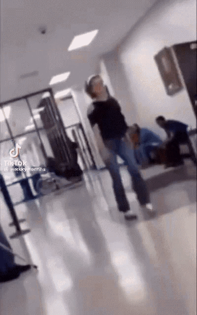 a woman is dancing in a hallway while a man sits on a bench in the background .