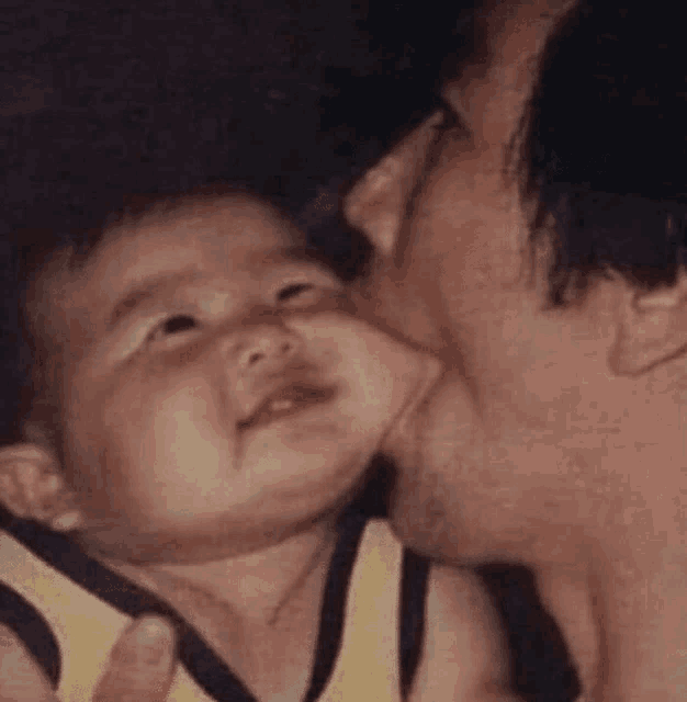 a man is kissing a baby on the cheek while the baby is smiling .