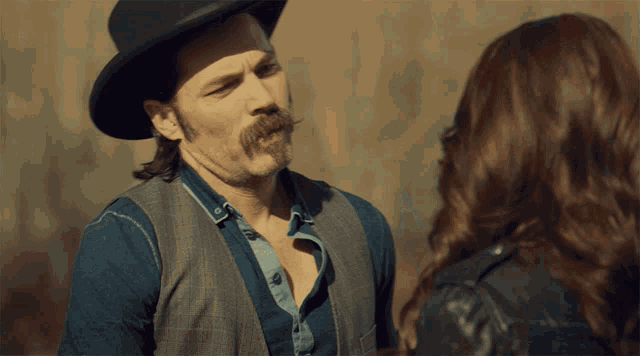 a man with a hat and a mustache looks at a woman