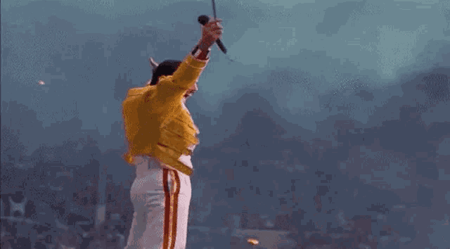 a man in a yellow jacket and white pants is dancing on a stage with a microphone .