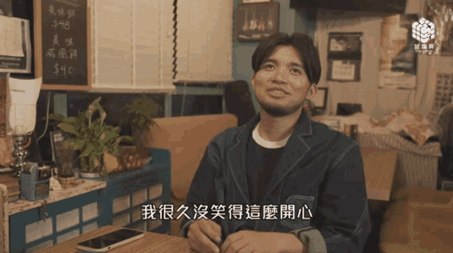 a man in a denim jacket sits at a table with a cell phone in his hand